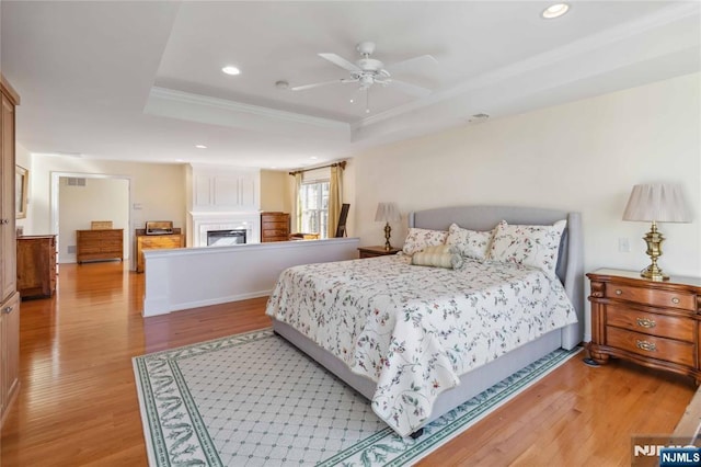 bedroom with recessed lighting, a tray ceiling, light wood-style floors, and a fireplace