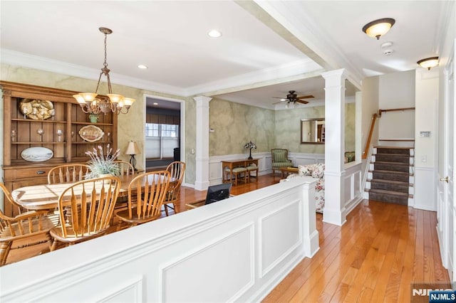 dining area with a wainscoted wall, light wood-style floors, crown molding, and ornate columns