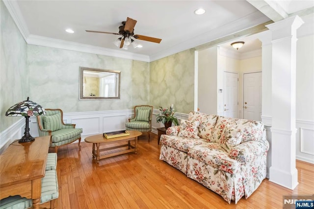 living room with a ceiling fan, wood finished floors, crown molding, a decorative wall, and decorative columns