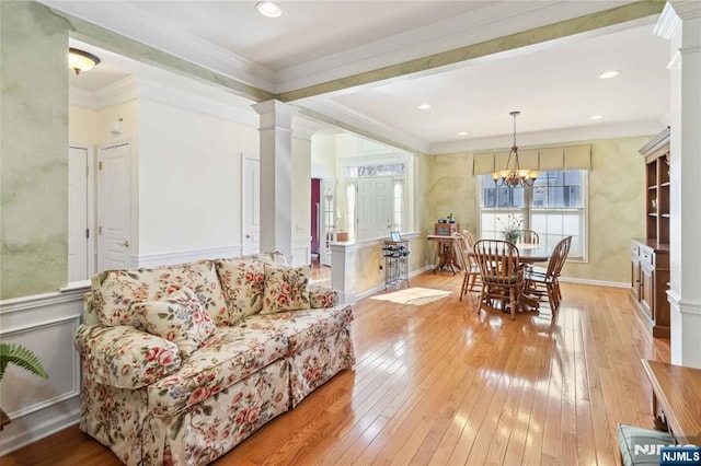 living room with light wood-type flooring, ornamental molding, recessed lighting, an inviting chandelier, and decorative columns