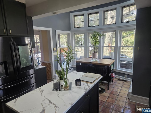 kitchen featuring light stone counters, black fridge with ice dispenser, dark cabinets, and a center island