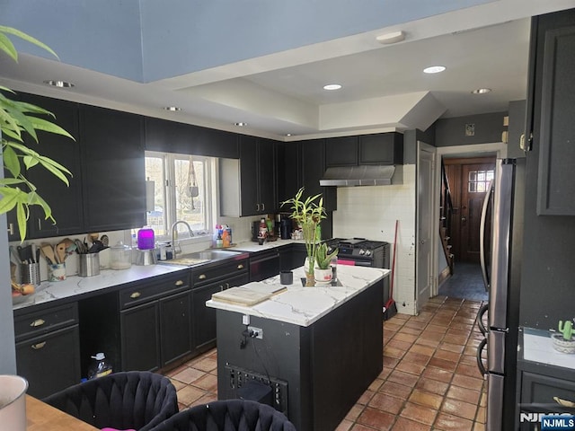 kitchen with a sink, under cabinet range hood, a kitchen island, freestanding refrigerator, and dark cabinets