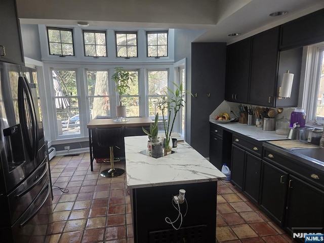 kitchen with dark cabinetry, visible vents, a baseboard radiator, a kitchen island, and black fridge with ice dispenser