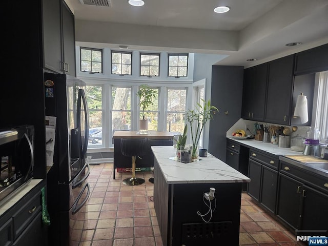 kitchen featuring visible vents, stainless steel microwave, black refrigerator with ice dispenser, dark cabinets, and a center island