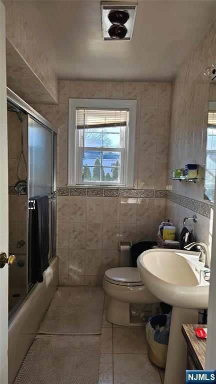 full bath with tile patterned flooring, toilet, tile walls, and shower / bath combination with glass door