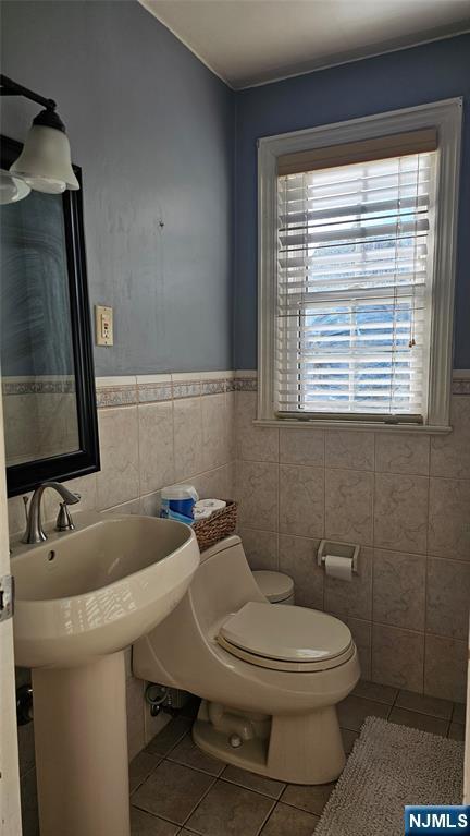 bathroom with toilet, tile walls, wainscoting, and tile patterned flooring