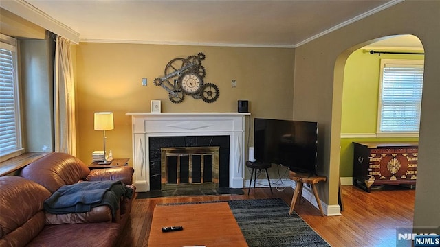 living area with baseboards, wood finished floors, ornamental molding, and a tiled fireplace