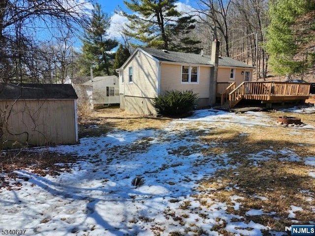 view of snowy exterior featuring a deck, a storage shed, and an outdoor structure