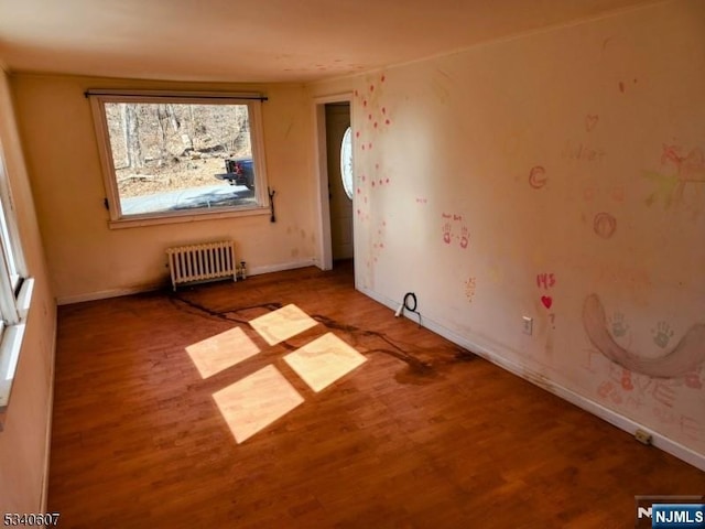 unfurnished room with radiator, wood finished floors, and baseboards