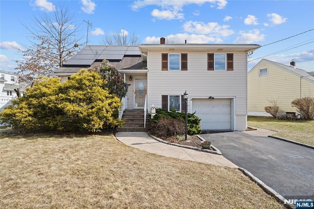 split level home featuring a front yard, solar panels, a chimney, a garage, and aphalt driveway