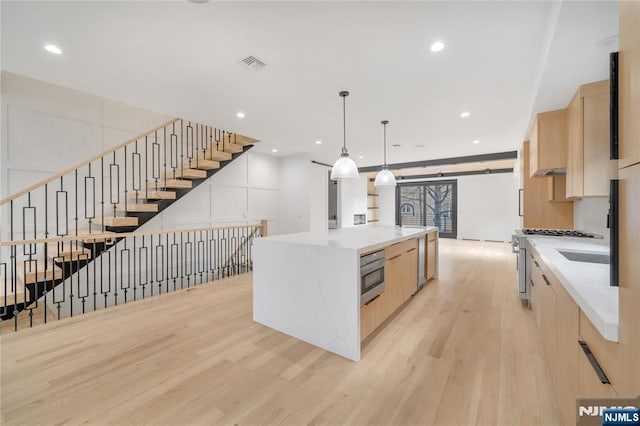 kitchen with oven, light brown cabinetry, a large island with sink, light wood-style floors, and modern cabinets