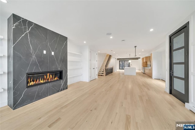 unfurnished living room featuring built in features, recessed lighting, stairway, light wood-style floors, and a fireplace