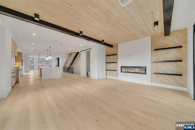 unfurnished living room with visible vents, a barn door, light wood-style floors, and stairway