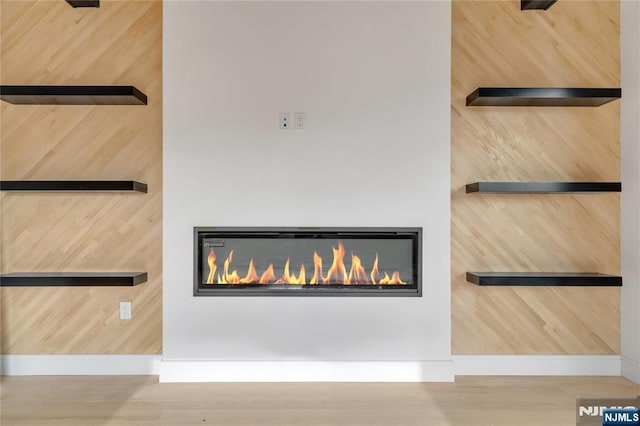 details featuring a glass covered fireplace, baseboards, and wood finished floors