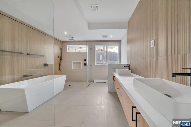 bathroom with visible vents, walk in shower, a soaking tub, tile walls, and a sink