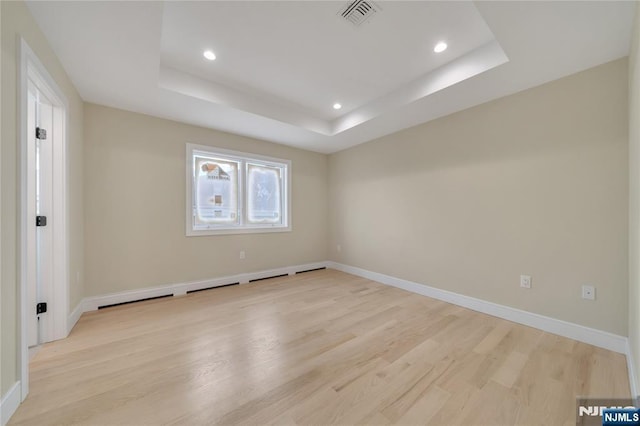 unfurnished room featuring visible vents, light wood-style flooring, a raised ceiling, and baseboards