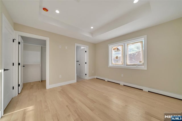 unfurnished bedroom featuring light wood-type flooring, a tray ceiling, recessed lighting, baseboards, and a spacious closet