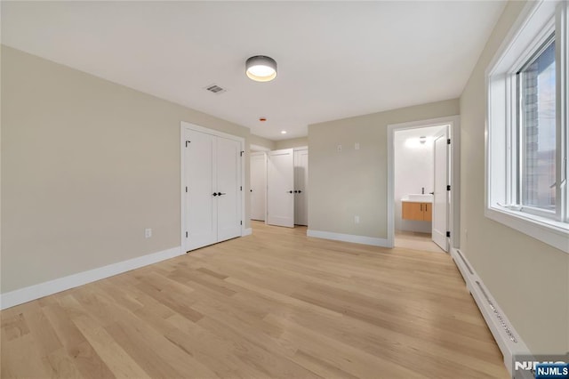 unfurnished bedroom with multiple windows, baseboards, baseboard heating, and light wood-type flooring