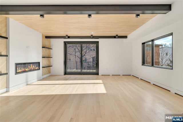 unfurnished living room featuring a glass covered fireplace, beamed ceiling, wood finished floors, and baseboards