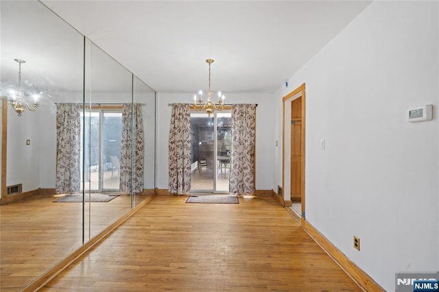 unfurnished dining area with visible vents, baseboards, an inviting chandelier, and wood finished floors