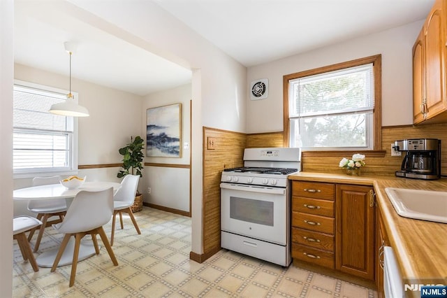 kitchen with white range with gas cooktop, brown cabinetry, light floors, and visible vents