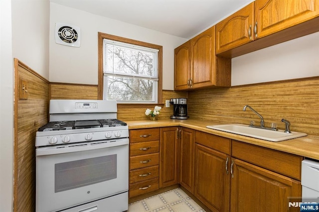 kitchen featuring a sink, white appliances, light floors, and brown cabinets