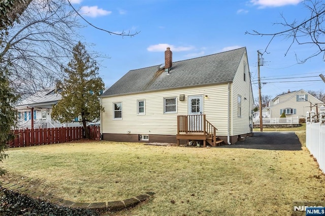 rear view of house with a lawn, a shingled roof, a chimney, and fence