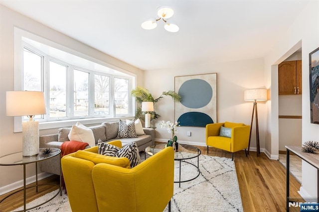 living area featuring light wood finished floors, an inviting chandelier, and baseboards