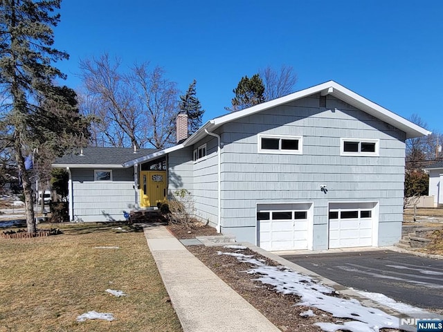 view of front facade featuring driveway, an attached garage, a chimney, and a front lawn