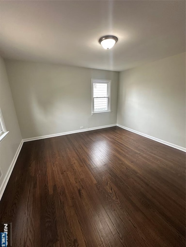 spare room featuring baseboards and dark wood finished floors