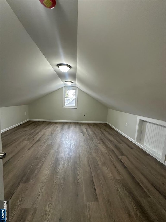 additional living space with baseboards, dark wood finished floors, and vaulted ceiling