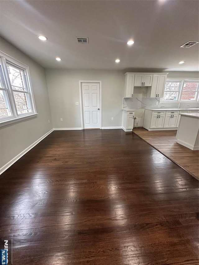 unfurnished living room featuring visible vents, plenty of natural light, dark wood-type flooring, and baseboards