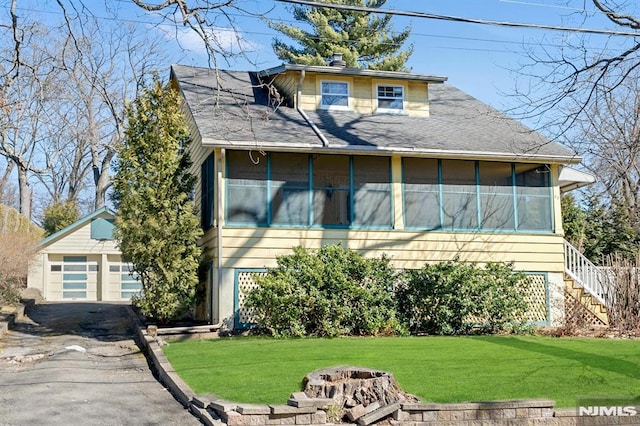 view of front of home featuring a front lawn, a detached garage, an outdoor fire pit, a sunroom, and a chimney