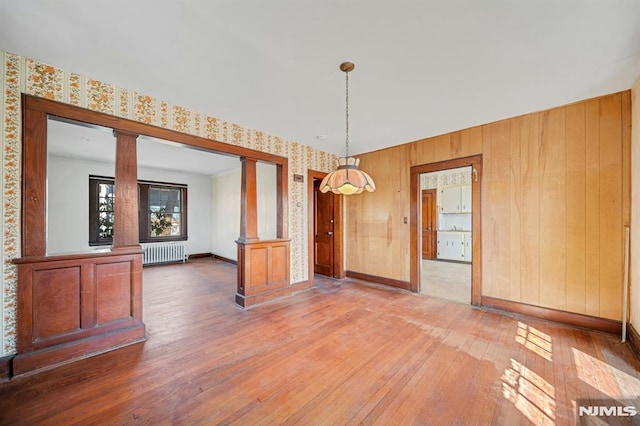 unfurnished dining area with hardwood / wood-style flooring, radiator, baseboards, and decorative columns