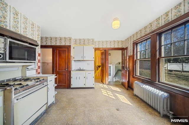 kitchen with stainless steel microwave, wallpapered walls, radiator heating unit, white range with gas cooktop, and white cabinetry