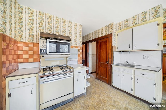 kitchen featuring wallpapered walls, light floors, white range with gas cooktop, white cabinets, and a sink