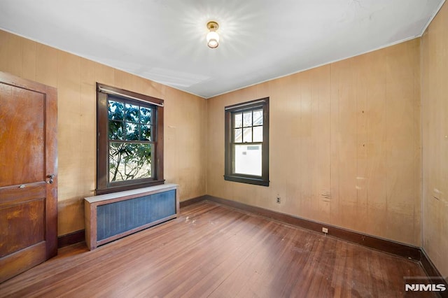 empty room with radiator heating unit, baseboards, and wood-type flooring