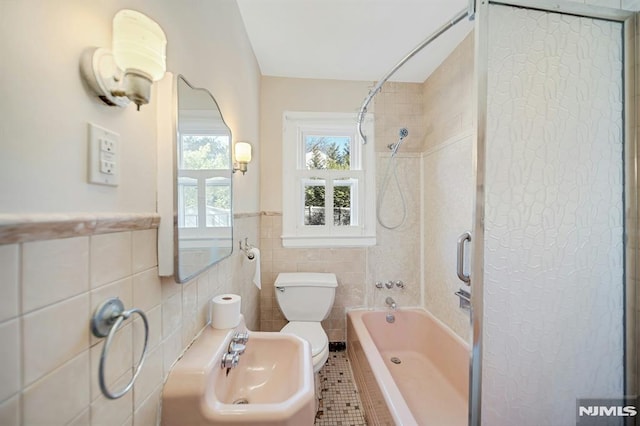 bathroom featuring a wainscoted wall, a sink, shower / washtub combination, tile walls, and toilet