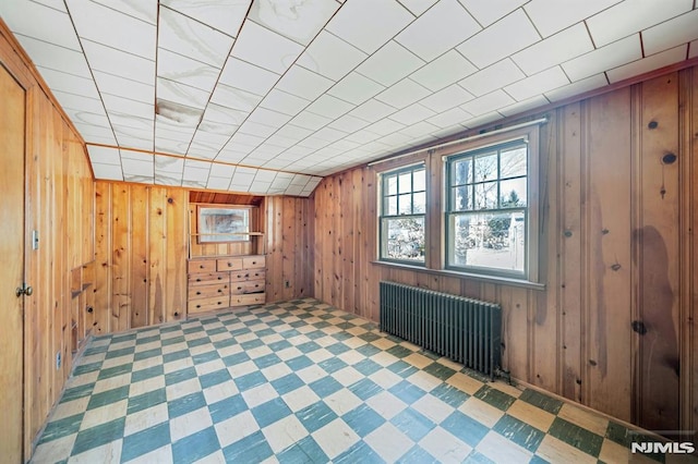 unfurnished room with lofted ceiling, radiator, and wood walls