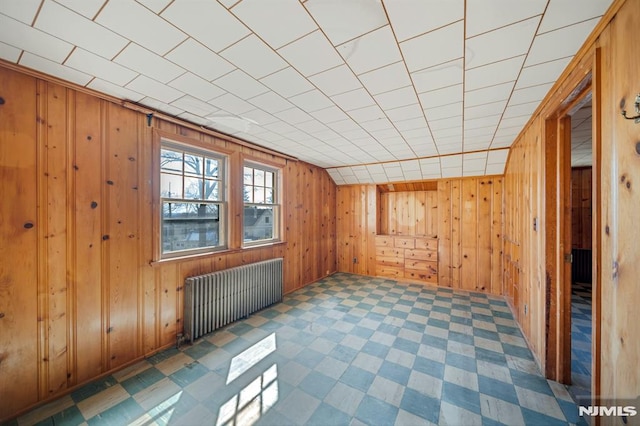 empty room featuring tile patterned floors, wooden walls, and radiator heating unit