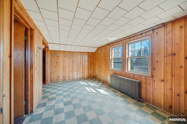 unfurnished room featuring tile patterned floors, wood walls, and radiator heating unit