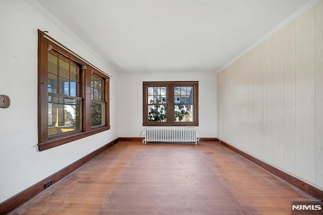 unfurnished room with radiator heating unit, wood finished floors, baseboards, and ornamental molding