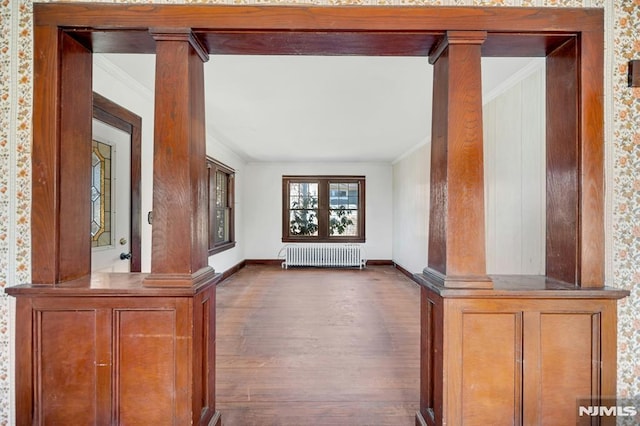 corridor featuring crown molding, radiator heating unit, wood finished floors, and ornate columns