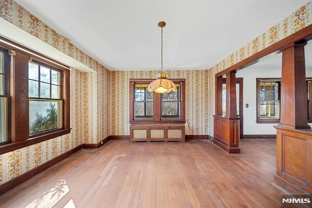 unfurnished dining area featuring decorative columns, radiator heating unit, and wallpapered walls