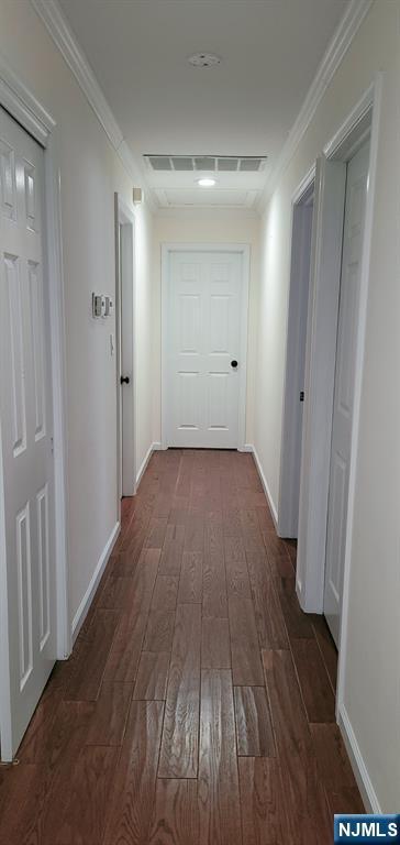 corridor featuring dark wood-style floors, visible vents, and ornamental molding