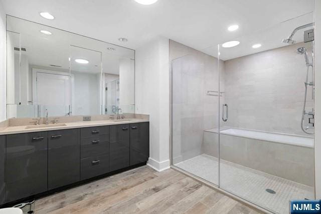 bathroom featuring double vanity, a stall shower, wood finished floors, and a sink