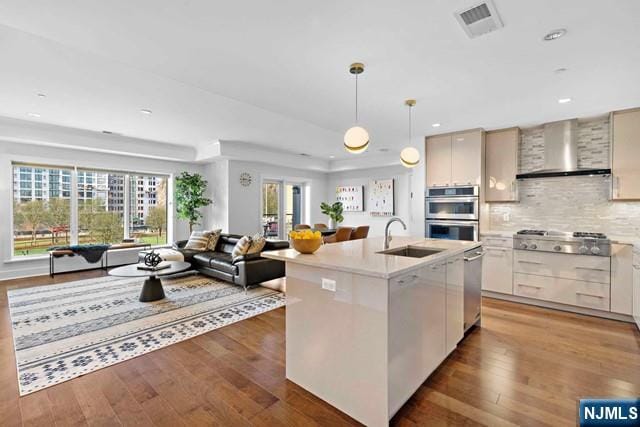 kitchen featuring visible vents, wall chimney range hood, open floor plan, stainless steel appliances, and a sink