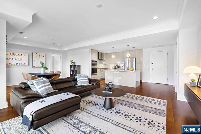 living area featuring recessed lighting, baseboards, a raised ceiling, and dark wood-type flooring