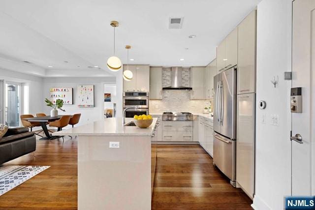 kitchen with wall chimney range hood, backsplash, wood finished floors, appliances with stainless steel finishes, and light countertops