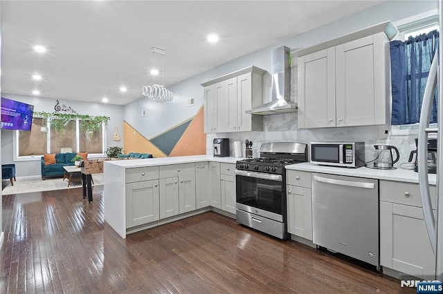 kitchen with open floor plan, stainless steel appliances, a peninsula, wall chimney range hood, and dark wood-style flooring